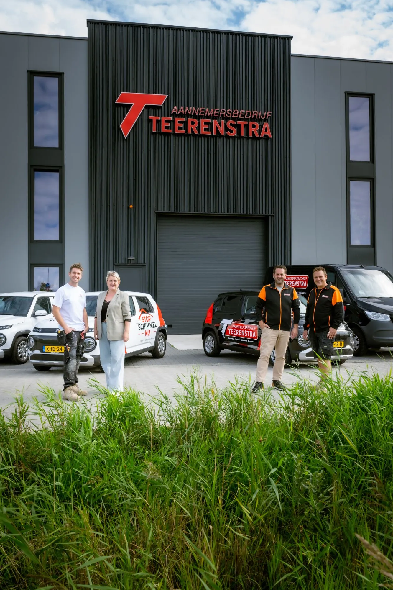 Vier mensen van Teerenstra en Stop Schimmel Nu voor het pand in Heiloo, met de bedrijfsauto's